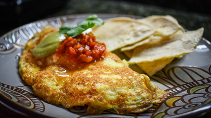 Egg omelette with red sauce, avocado sauce and corn tortilla chips.