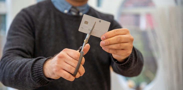 man holding credit card cut into halves and looking happy debt payout. cutting credit card. Man cutting debit card scissors Hands of man cutting a credit card with scissors. financial problems at home