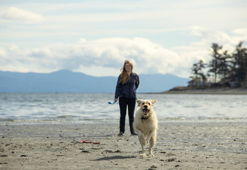 woman on the beach with dog running in the sand toward camera