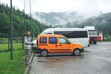 Fototapeta premium The guy in a sports suit near the orange car. Man on mountains background.