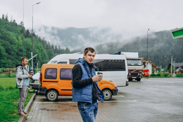 Two young men near the car. Men drink coffee