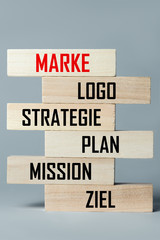 A list of wooden blocks lying on top of each other with a list of components of a successful business and brand in German, in the translation of the word: brand, logo, strategy, plan, mission, target