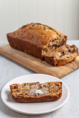 Slice of banana bread with butter melting, loaf in background
