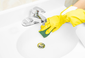 Woman in yellow rubber gloves is cleaning bathroom sink with detergent