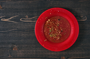Salad leftovers after meal. Oil, tomato seeds, chopped parsley on a single red plate. Wooden table background. Top down flat photo with copy space