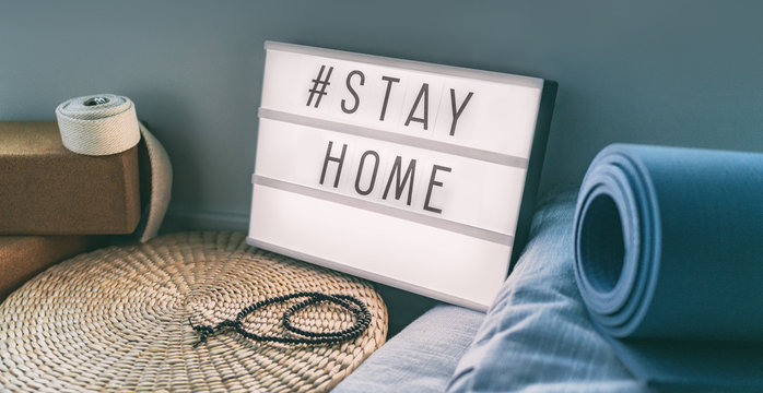 Coronavirus Yoga at home sign lightbox with text hashtag #STAYHOME glowing in light with exercise mat, cork blocks, strap meditation pillows. COVID-19 banner to promote self isolation staying at home.