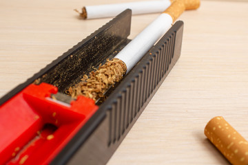 machine for stuffing cigarettes and cigarettes in the background on a light wooden