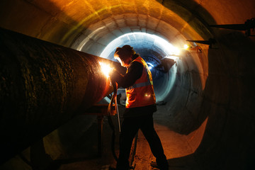 Worker in protective mask welding pipe in tunnel