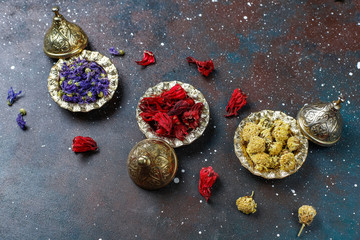 Assortment of dry tea in golden vintage mini plates.Tea types background:hibiscus,chamomile,mixed black tea,dry roses,butterfly pea tea