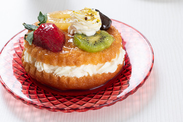 Baba with rum syrup with fresh fruits, strawberry, kiwi, pineapple slice and whipped cream