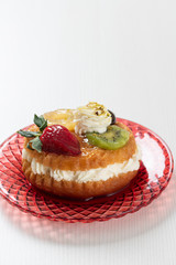 Italian sweet Baba of Naples with rum syrup with fresh strawberries, kiwis, pineapple and whipped cream