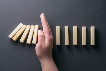 Top view man hand stopping falling dominos in a business crisis management conceptual image