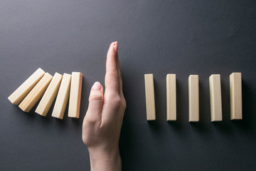 Top view whomen hand stopping falling dominos in a business crisis management conceptual image