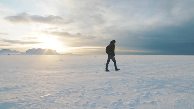 Young man traveler walking on snow desert in Iceland. Slow motion shot at sunset or sunrise. Around Solheimasandur dc3 Plane crash area 