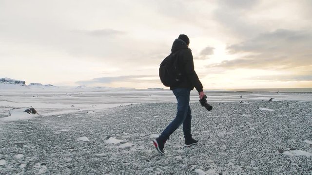 Young man traveler with camera walking on snow desert in Iceland. Slow motion shot at sunset or sunrise. Around Solheimasandur dc3 Plane crash area 