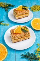 Orange cake decorated with fresh orange slices and mimosa flowers on light background