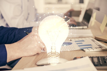 Double exposure of man's hands holding and using a digital device and bulb hologram drawing. Idea concept.