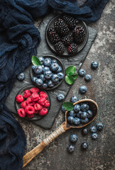 Fresh berries with raspberries, blueberries, blackberries in bowl on a stone stand on a dark metal background.