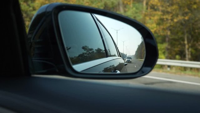 Close-up Side-view mirror Reflection Car Moving Behind Following on Highway. Bright Sunny Summer Autumn Morning Day, Blue Sky. 2x Slow motion 0.5 speed 60 FPS