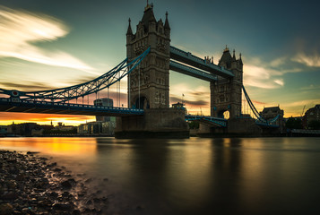 Tower Bridge located in London city, United Kingdom with beautiful sunset afternoon blue sky background. Calm River Thames in long exposure shot with tourism, tourist view in city landscape	