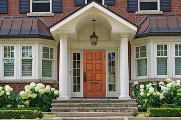 Fototapeta na wymiar Front door of traditional two story house with portico entrance and hydrangea flowers