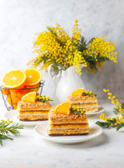 Orange cake decorated with fresh orange slices and mimosa flowers on light background