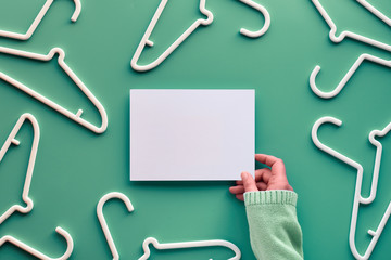 White plastic hangers, hand holding white paper with copy-space. Top view flat lay on trendy pastel...