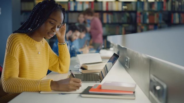 University Library: Gifted Black Girl uses Laptop, Writes Notes for the Paper, Essay, Study for Class Assignment. Diverse Multi-Ethnic Group of Students Learning, Studying for Exams, Talk in College