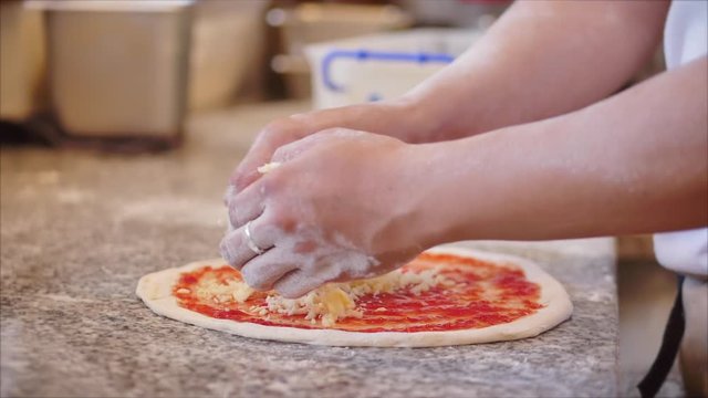 A real pepperoni pizza, a method of its preparation, the Italian chef cooks with his fingers a real Italian pizza from the dough, sprinkling pizza with mazzarella cheese.
