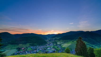 Fototapeta na wymiar Panorama of beautiful skyline in a valley town at dawn, green hills and peaceful Münstertal 