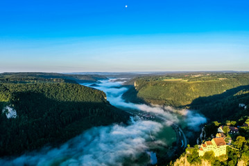 View of cloud-covered Danube valley from Knopfmacherfelsen, Beuron, Germany; Monastery on green hill under blue sky