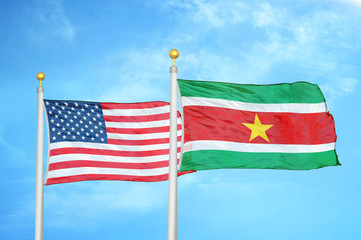 United States and Suriname two flags on flagpoles and blue cloudy sky