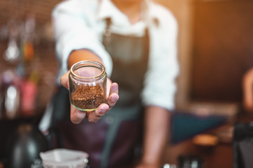Close up of hands barista man Holding a coffee bean that has been ground. male hands placing a cup of coffee on table. Coffee, Barista, extraction, serve, cafe, lifestyle concept.