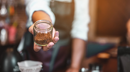 Close up of hands barista man Holding a coffee bean that has been ground. male hands placing a cup of coffee on table. Coffee, Barista, extraction, serve, cafe, lifestyle concept.