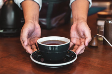 Close up of hands barista man serving coffee in coffee shop. male hands placing a cup of coffee on table. Coffee, Barista, extraction, serve, cafe, lifestyle concept.