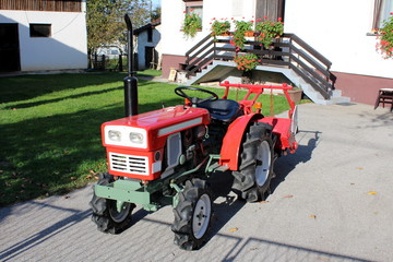 Restored and completely renovated vintage retro old small compact utility tractor with new tyres parked on paved driveway of suburban family house surrounded with grass and flowers