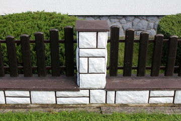 Side view of dark brown wooden picket fence mounted on concrete foundation covered with white stone...