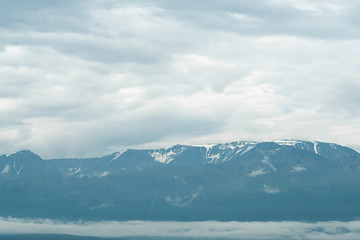 Fototapeta na wymiar snow peaks on horizon, ridge of rocks under cloudy sky in mountain valley