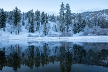 mountains and forest reflecting in lake during winter