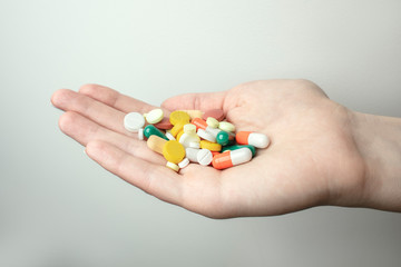 A handful of various pills in a woman's hands. Medications against the COVID-19 and other conditions and diseases on the grey background. Medicine.