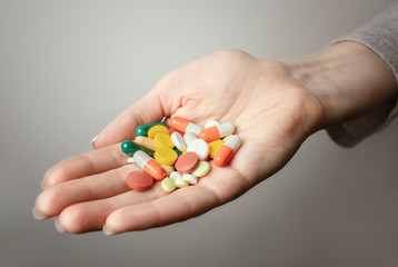 A handful of various pills in a woman's hands. Medications against the COVID-19 and other conditions and diseases on the grey background. Medicine.