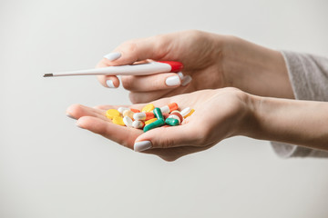 A handful of various pills with a digital thermometer in a woman's hands. Medications against the COVID-19 and other conditions and diseases on the grey background. Medicine.