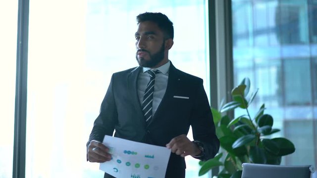 Experienced formally dressed corporate director holding paper report for explaining information during working process in office interior,Turkish executive manager talking during brainstorming meeting