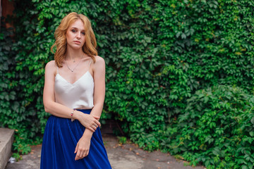 Portrait of a young beautiful woman, standing next to the wall of wild grape leaves.