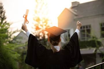Back of view Graduate put hands up and celebrating with certificate in her hand and so proud and...