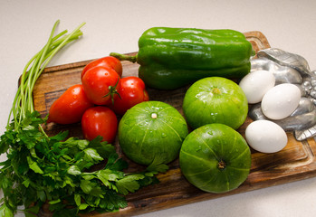 Wooden table with some vegetables, zucchinis, tomatoes, parsley, green pepper  and eggs.