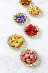 Assortment of dry tea in golden vintage mini plates.Tea types background:hibiscus,chamomile,mixed black tea,dry roses,butterfly pea tea