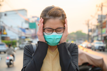 Woman having headache and wearing surgical mask for protect bad air pollution or virus. Headache maybe occurs from stress, tension or migraine etc.