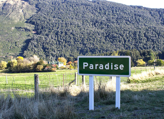 Sign "Paradise" in a scenic valley against backdrop of mountains