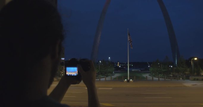 Photographer snaps picture of saint louis arch at night, cinematic slow motion over the shoulder shot with rack focus
